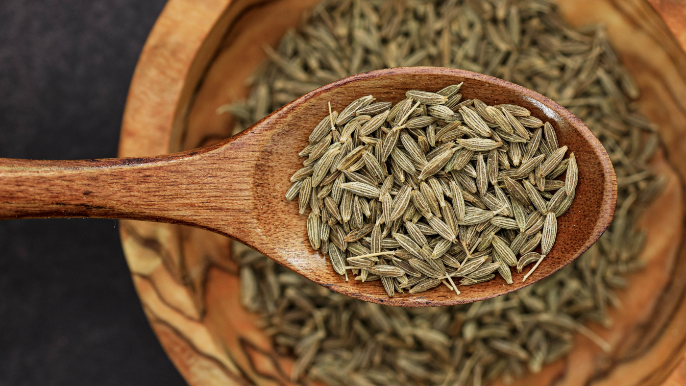 an image of a spoon full of cumin with a bowl full of cumin seeds in the background indicating the cumin health benefits
