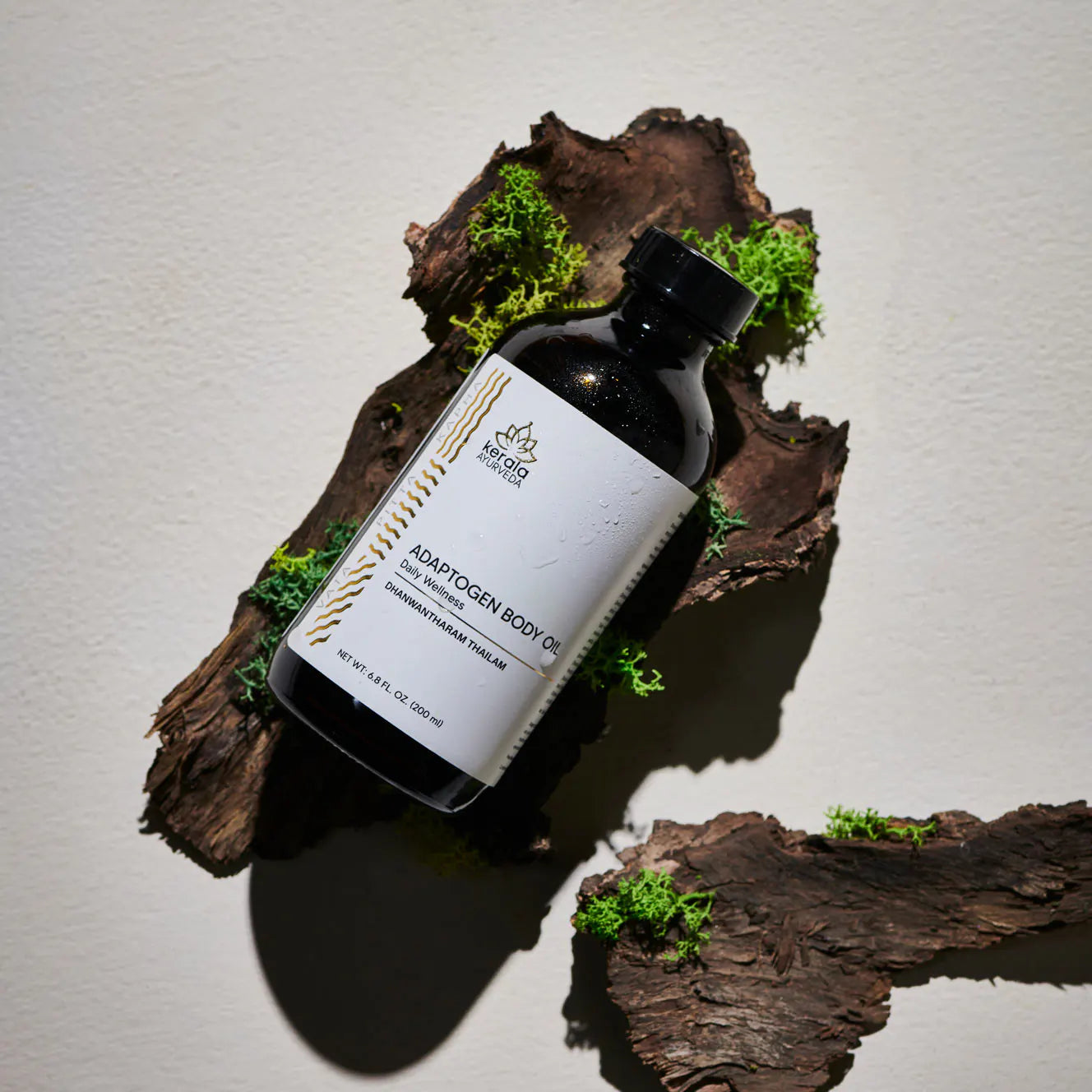 Black bottle of Adaptogen Body Oil on natural wood with green moss accents against a neutral background.