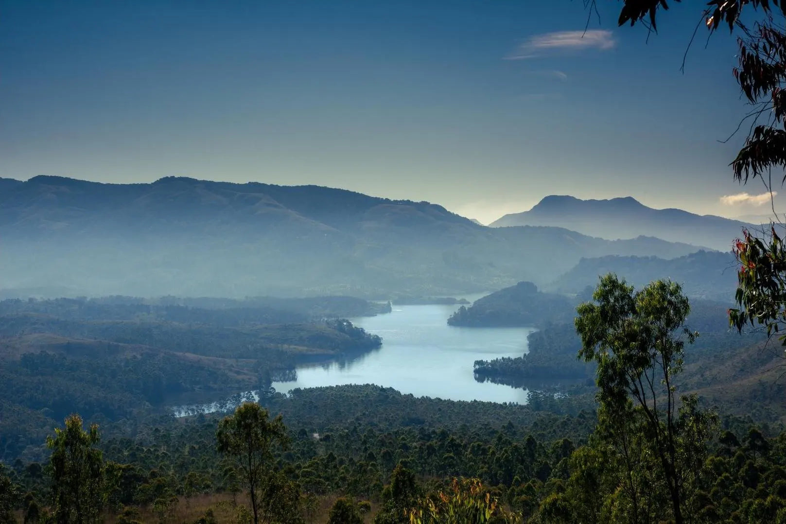 A peaceful landscape featuring a river winding through mountains and forests under a clear blue sky.