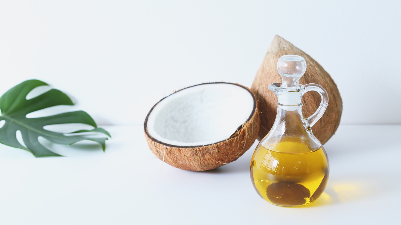 an image of coconut oil in a container with 2 coconuts places next to the oil, in a white background
