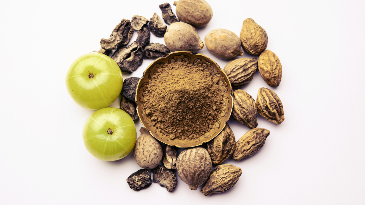 an image of tripahal powder in a bowl with amla and triphala nuts in the background
