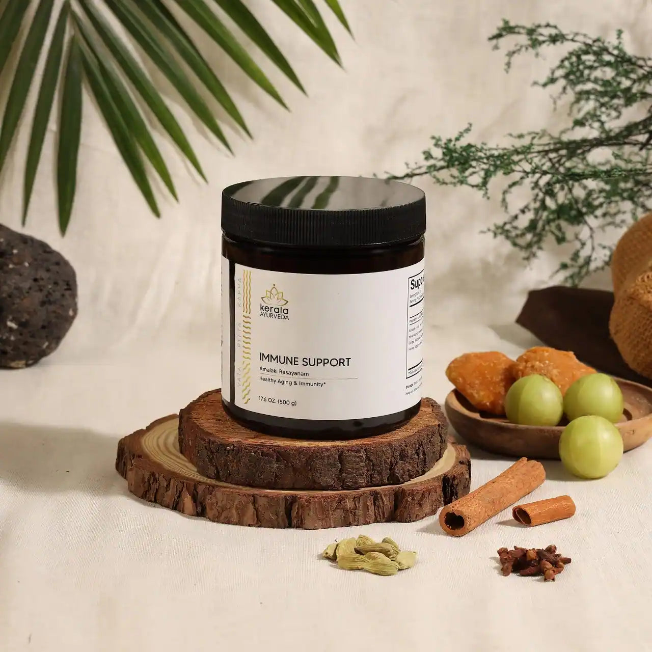 A jar of Kerala Ayurveda Immune Support, Amalaki Rasayana, with a label indicating it is a product for healthy aging and immunity, weighing 17.6 oz / 500 g. The jar is placed on the wooden costers with spices around.