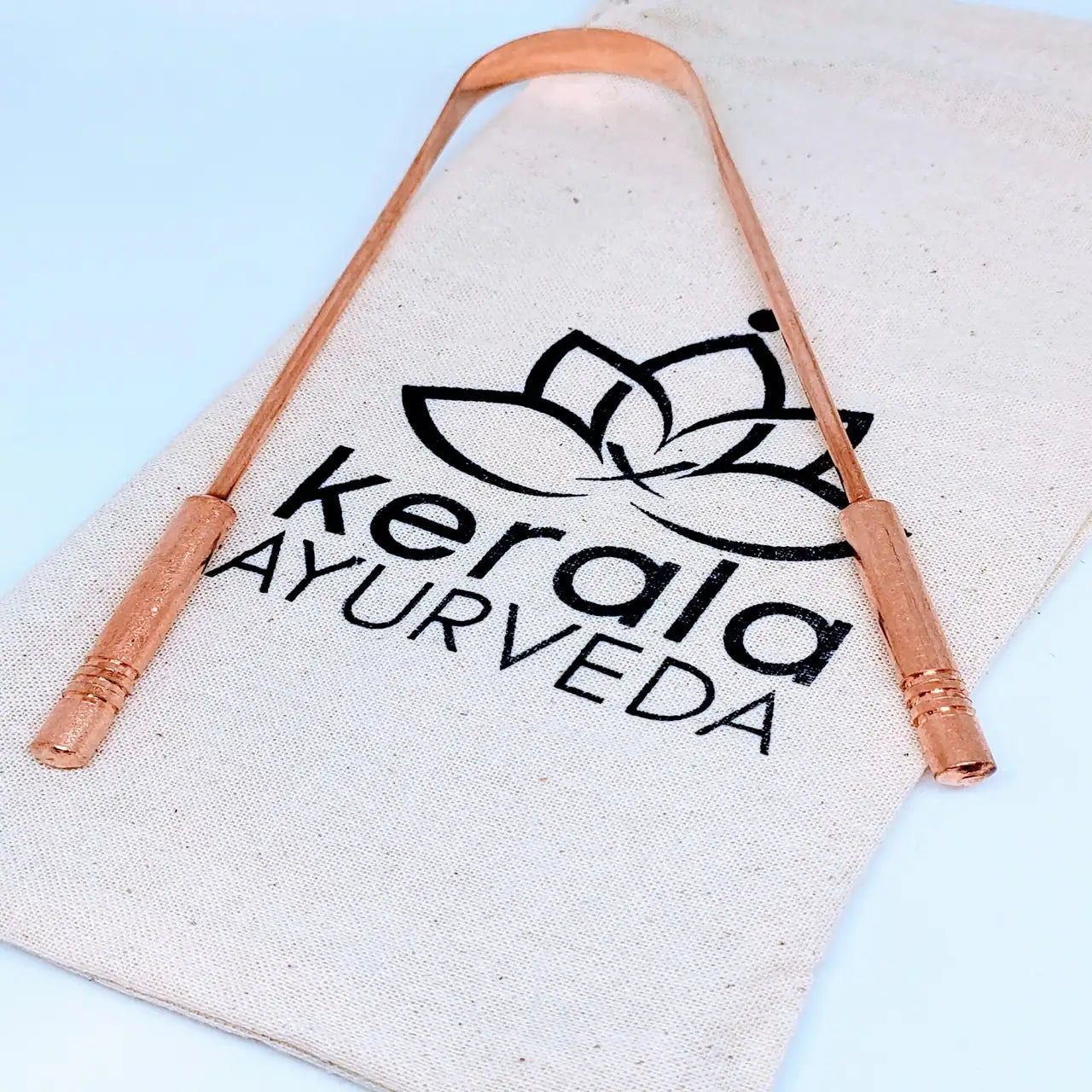 A copper tongue cleaner with a branded Kerala Ayurveda packaging in the background.
