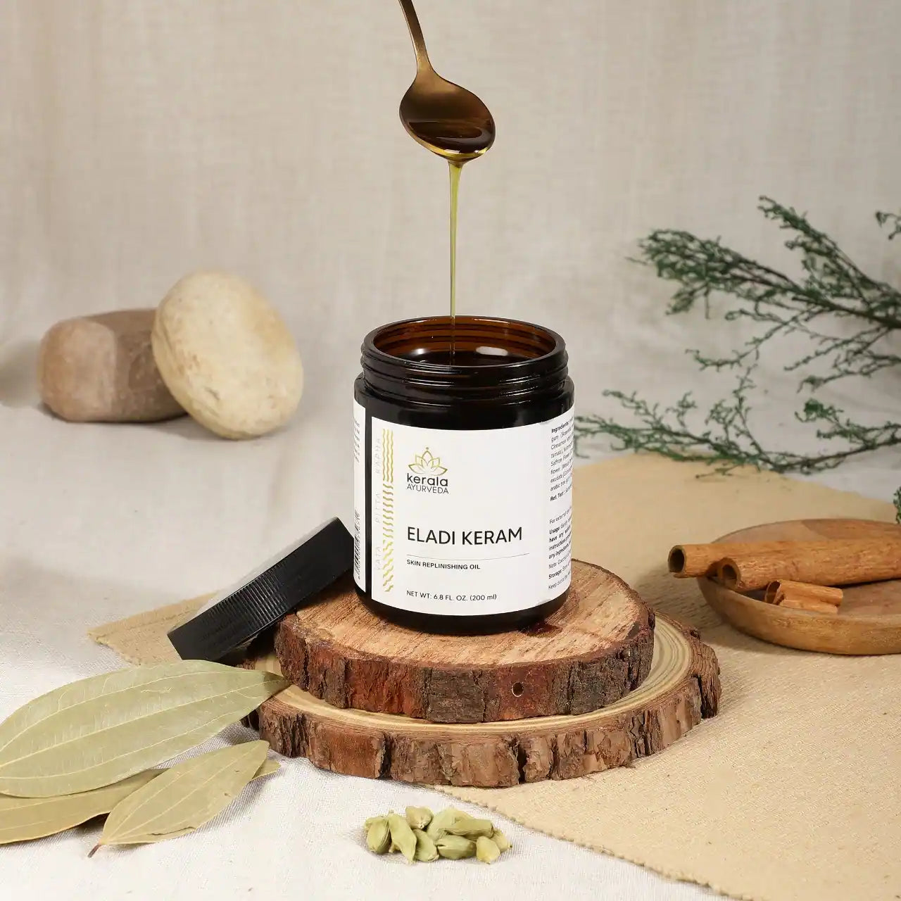 An open Box of Kerala Ayurveda Eladi Keram, a herbal massage oil, with a capacity of 200 ml on a wooden coster and beige background with spices around.