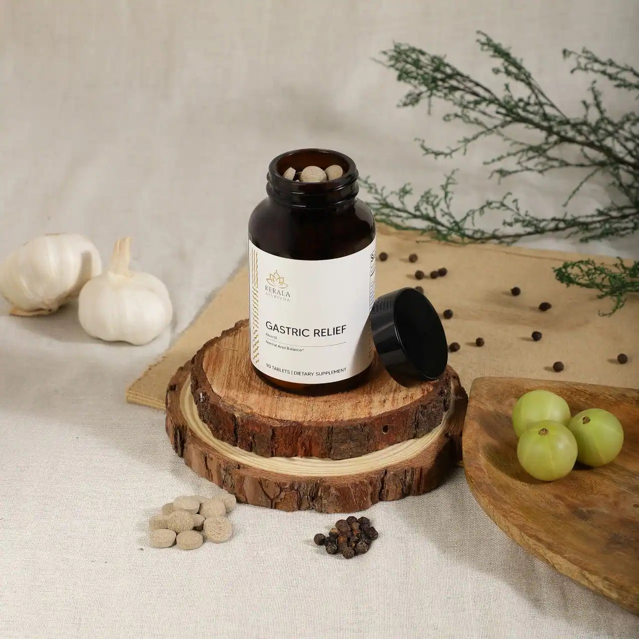 An open bottle of Kerala Ayurveda Gastric Relief, containing 90 tablets for dietary supplement, with spices and capsules lying around the bottle