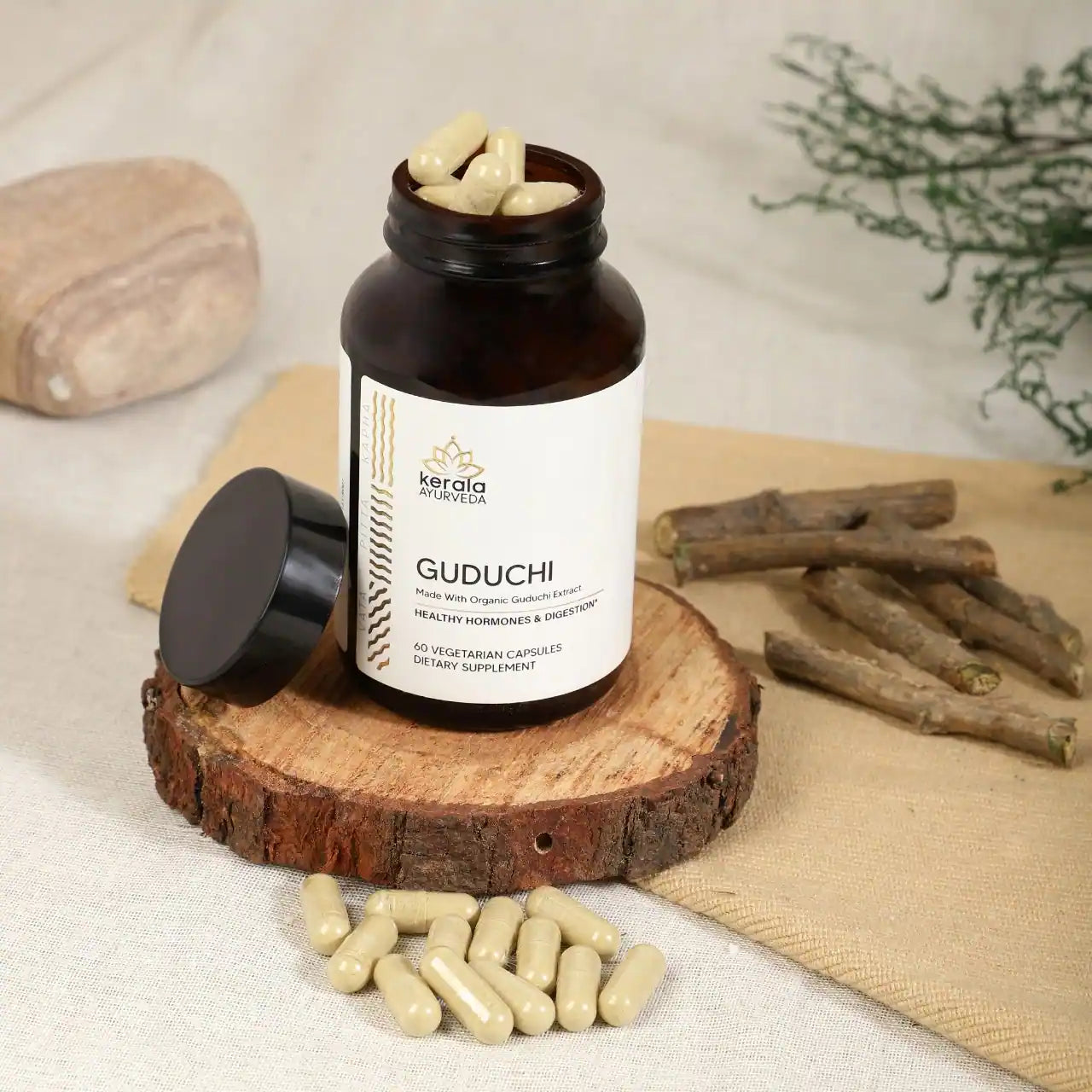 An open bottle of Kerala Ayurveda Guduchi capsules placed on the wooden coster with spices and capsules beige background