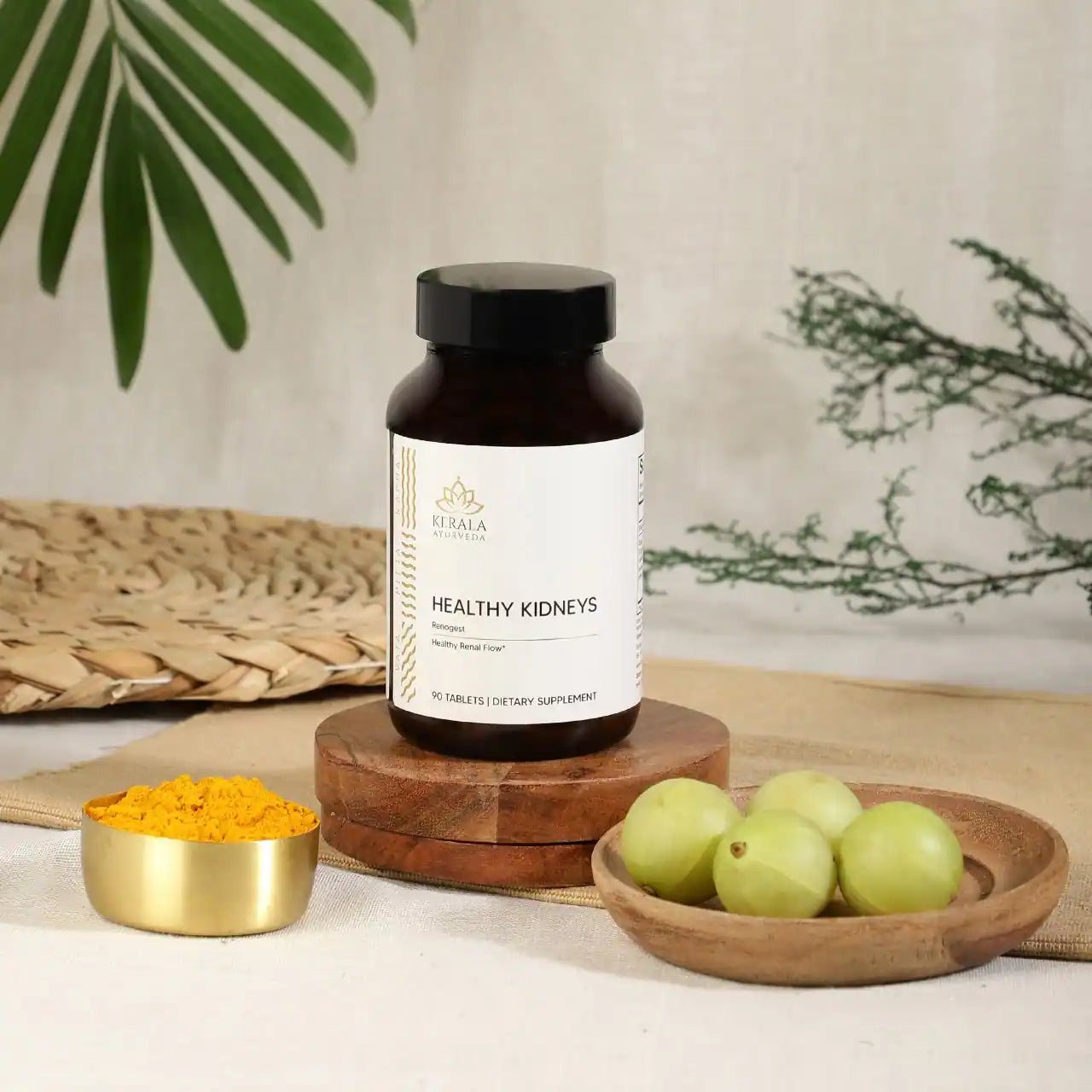 A bottle of Healthy Kidneys dietary supplement with 90 tablets, labeled as Renogest, by Kerala Ayurveda. The bottle is places in a beige background with turmeric and gooseberries lying around