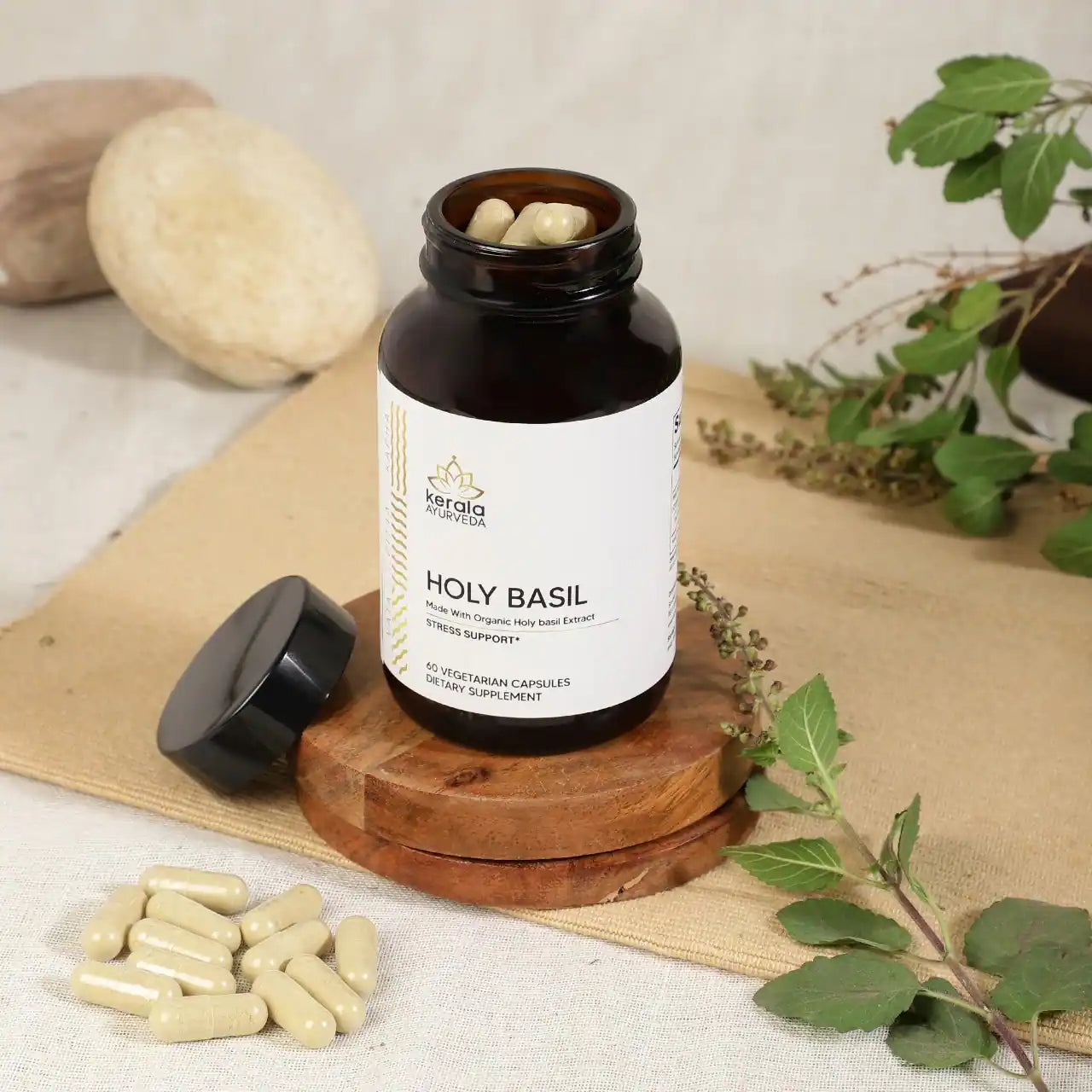 A open bottle of Kerala Ayurveda Holy Basil dietary supplement with 60 vegetarian capsules, labeled as stress support in beige background with capsules lying around