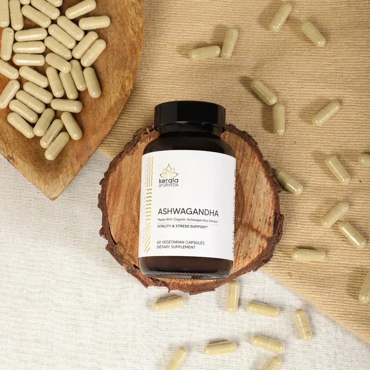 A bottle of Kerala Ayurveda Ashwagandha dietary supplement with 60 capsules, llying on a wooden coster with beige background and capsules
